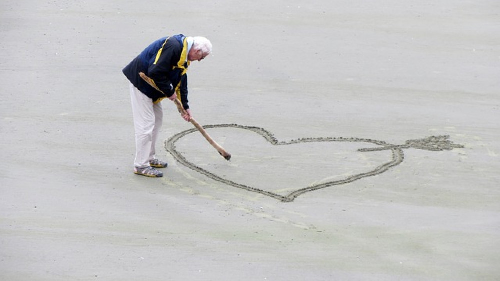 Ein Senior malt ein Herz am Strand (Symbolbild). Soziale Sicherheit im Alter bleibe eine der drängendsten Herausforderungen, argumentiert Ergo-Chef Achim Kassow.