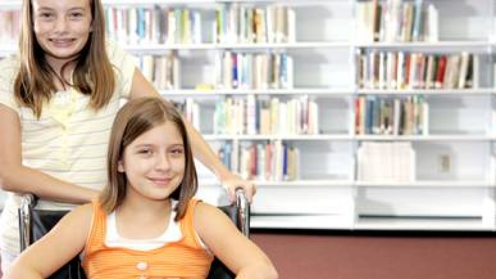 Two school girls at the library. One is in a wheelchair.